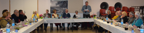 Photo des participants au Burn's supper assis à table, le présidents Pierre Delignière 
						est debout en train de lire un texte.