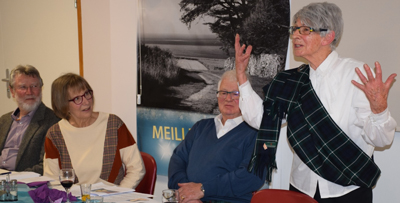 Photo of participants in Burn's supper seated at the table, a member speaks standing.