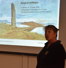 Anne Dietrich en buste, devant l’écran à gauche, où sont 
					projetées les diapositives illustrant le propos de l’intervenante sur l’Âge Néolithique aux îles Orcades.